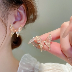 Détail de boucles d'oreilles papillon en cristal rose et doré sur l'oreille et main