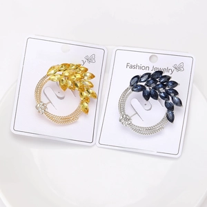 Close-up of golden and silver floral cluster brooches with marquise gems on white card