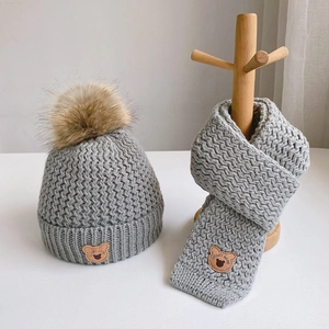 Detail of light grey knit hat and scarf set with pompom and cute bear patches