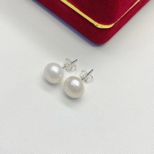 Macro shot of white pearl earrings with S925 silver studs on a white leather surface