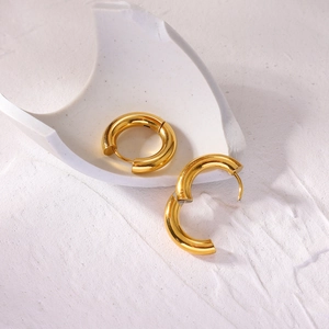 Detailed close-up of 4mm thick gold stainless steel hoop earrings on textured white surface