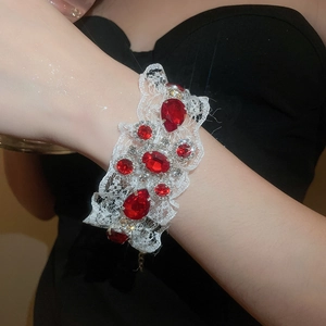Détail du bracelet en dentelle blanche avec pierres rouges en forme de goutte et strass brillants