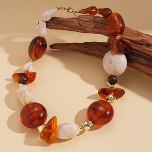 Détail de perles en acrylique ambre et crème sur une branche de bois sombre et épurée