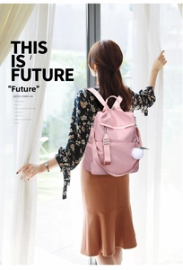 Pink nylon backpack with white fuzzy ball charm shown from behind on a model