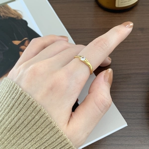 Detail of minimalist gold wavy silver ring with a single zircon worn by a model