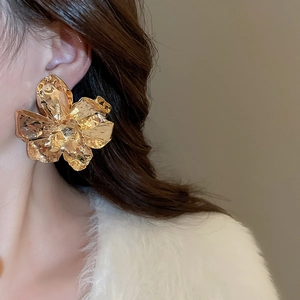 Close-up of model wearing large golden flower earrings with hammered metal texture