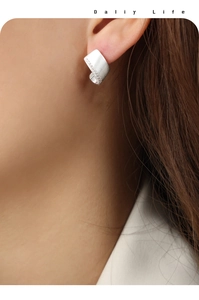 Detail of silver geometric stud earrings with matte finish worn by a female model