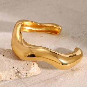 Moderner minimalistischer gewellter Armreif aus goldpoliertem Edelstahl auf Marmor