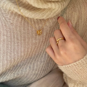 Detail of golden geometric cylinder necklace and ring set on beige knitted sweater