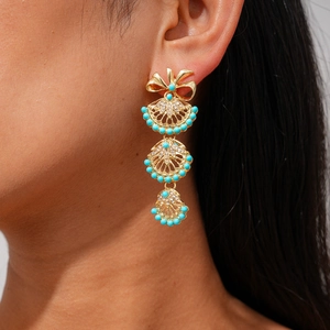 Close-up of golden bow earrings with fan-shaped turquoise pendants on a model