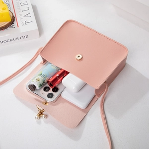 Pink faux leather crossbody bag with pearl charm showing capacity for phone and lipstick