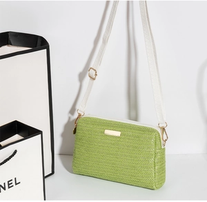 Close-up of green woven straw texture with gold zipper and white strap on crossbody bag