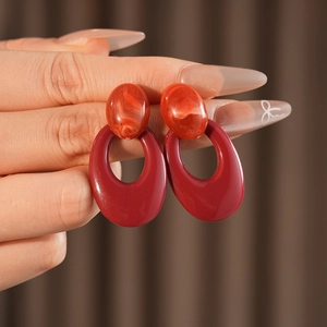 Close-up of red resin oval earrings with marble texture held by a hand on brown fabric