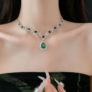 Close-up of V-shaped silver necklace with green teardrop crystal and small diamonds