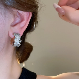 Close-up of sparkling silver C-shaped hoop earrings with zircon stones on a model