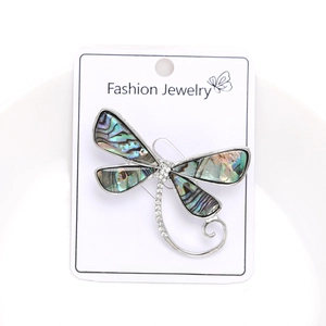 Macro shot of dragonfly brooch with abalone shell wings and sparkling crystals on white dish