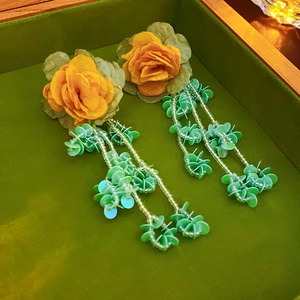 Gros plan de boucles d'oreilles fleur en tissu jaune avec glands perlés verts sur plateau