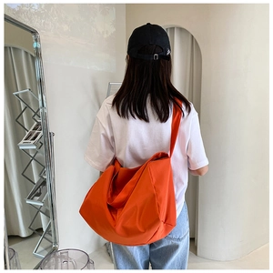Back view of a large orange oxford cloth messenger bag worn on model for casual styling