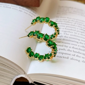 Primo piano di orecchini di cristallo verde smeraldo con cerchi in oro a C su un libro