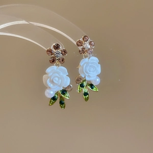 Macro shot of floral earrings with champagne crystals white resin rose and faux pearl detail
