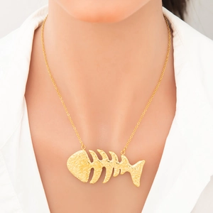 Detailed view of an 18k gold fishbone pendant necklace worn on a white shirt
