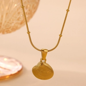 Macro detail of golden seashell pendant necklace with textured ridges on a fine chain