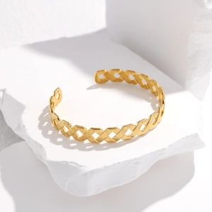 Detail of gold C-shaped titanium steel bracelet with geometric hollow woven texture