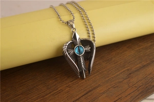 Détail du pendentif aile d'ange argenté avec croix et œil maléfique bleu sur chaîne