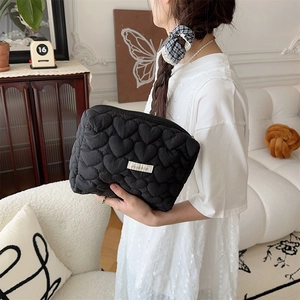 Detail of black heart quilted makeup bag with brand label held by a model