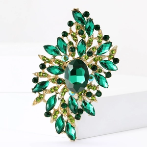 Close-up of vintage gold brooch with green crystals on white geometric stand