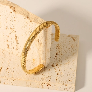 Detail of 18K gold plated knotted cuff bracelet on a natural beige travertine stone