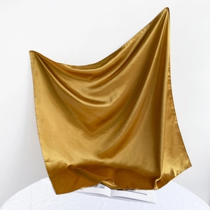 Elegant gold satin square scarf hanging gracefully over a white book and table
