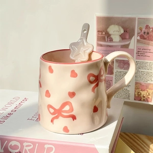 Cute ceramic mug with pink bow heart patterns and star spoon in soft sunlight