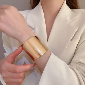 Detail of a wide gold metal cuff bracelet with a polished finish worn on a wrist