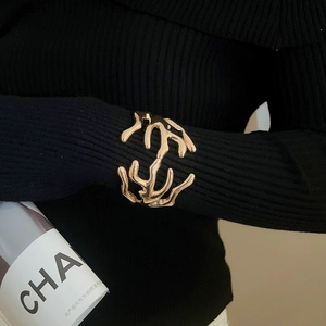 Detailed view of an organic lava-style gold cuff bracelet over black ribbed knit fabric
