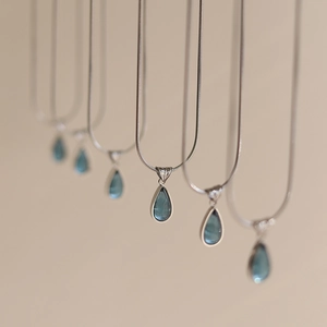 Macro view of teardrop blue ocean pendant necklaces with polished silver snake chains