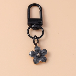 Detail view of a black metal keychain hook with a dark grey flower charm and gold edges