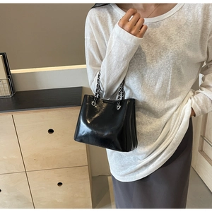Chic black glossy leather bucket bag with silver metal chain strap shown on a shoulder