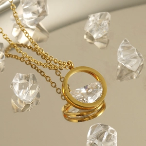 Collier en acier inoxydable doré avec pendentif cristal rond sur surface réfléchissante