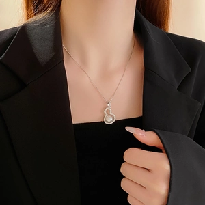 Detail of zircon gourd and pearl pendant necklace on a model showing delicate silver chain