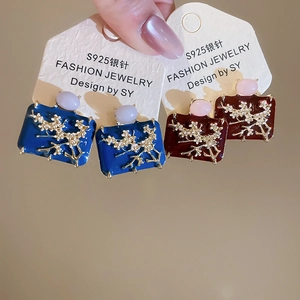 Detail of square enamel stud earrings with golden plum blossom patterns in blue and red