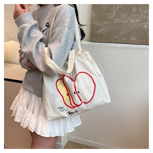 Detail of a cream canvas tote bag featuring a red apple graphic and drawstring closure
