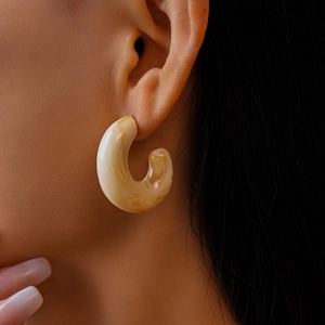 Close-up of beige acrylic C-shaped earrings with marble texture on female model