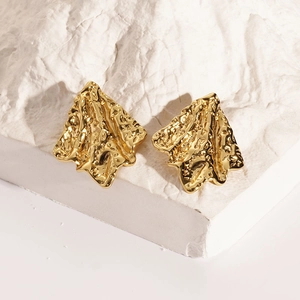 Detailed close-up of gold irregular geometric earrings with textured lava surface on a rock