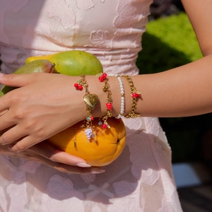 Gold layered bracelets with pearls and fruit charms on wrist in outdoor setting