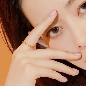 Close-up of a minimalist golden plain band ring worn on a model's finger with soft lighting