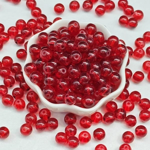 Close-up of translucent red glass beads for DIY jewelry in a white petal tray