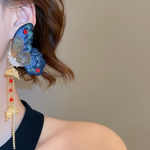 Détail de la boucle d'oreille papillon brodée avec glands dorés et perles sur modèle