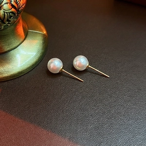 Elegant pearl stud earrings with gold plating on a textured dark leather surface