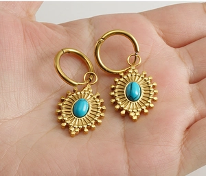 Détail de boucles d'oreilles soleil dorées avec incrustation de turquoise bleue